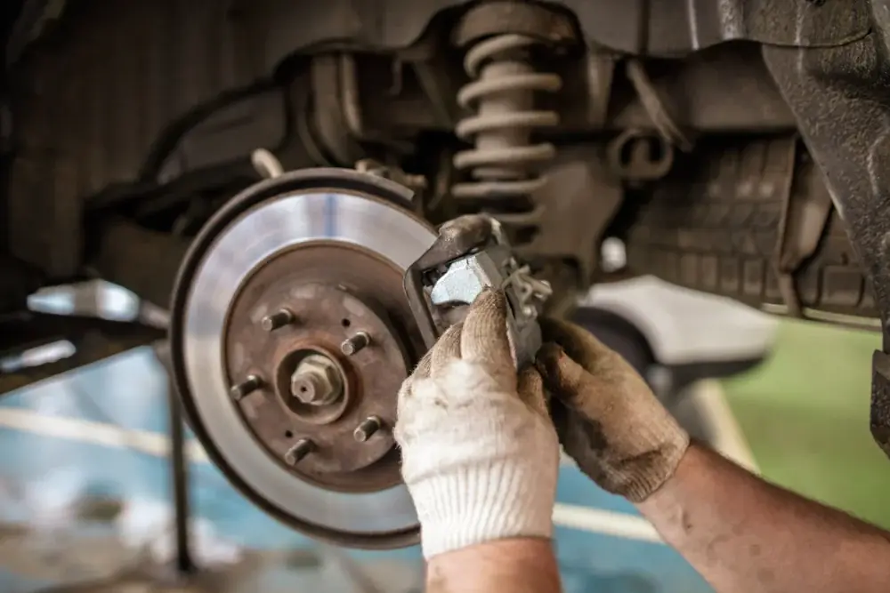 A mechanic fitting a brake caliper to a disc, with the suspension strut visible above