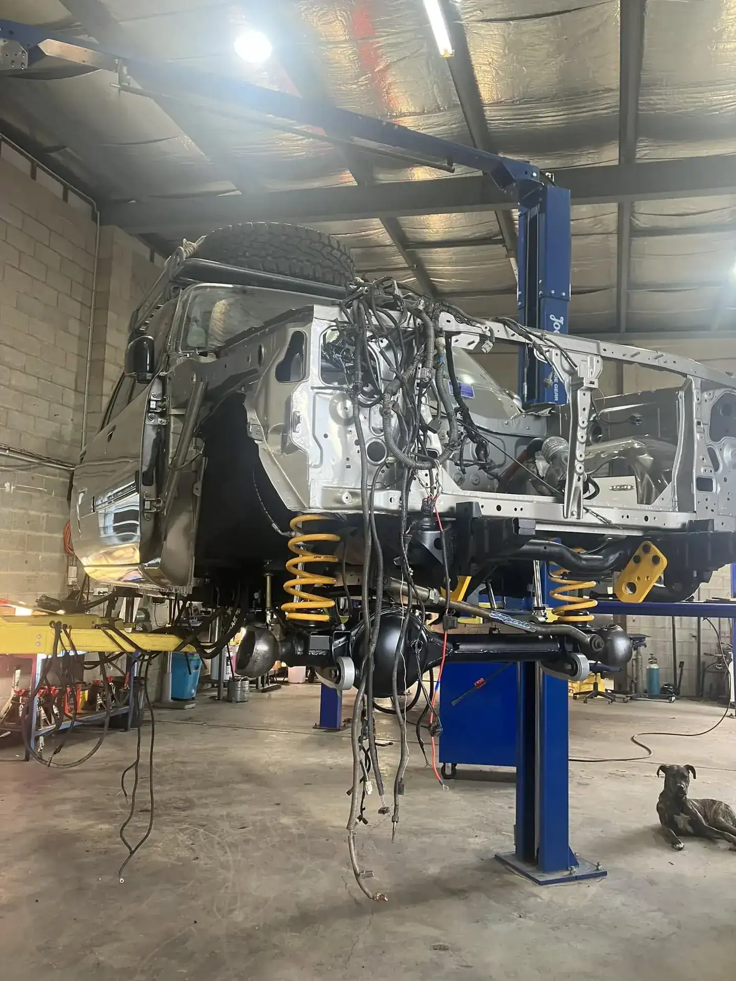 A 4WD chassis stripped down and raised on a two-post hoist inside the SJB Mechanical workshop